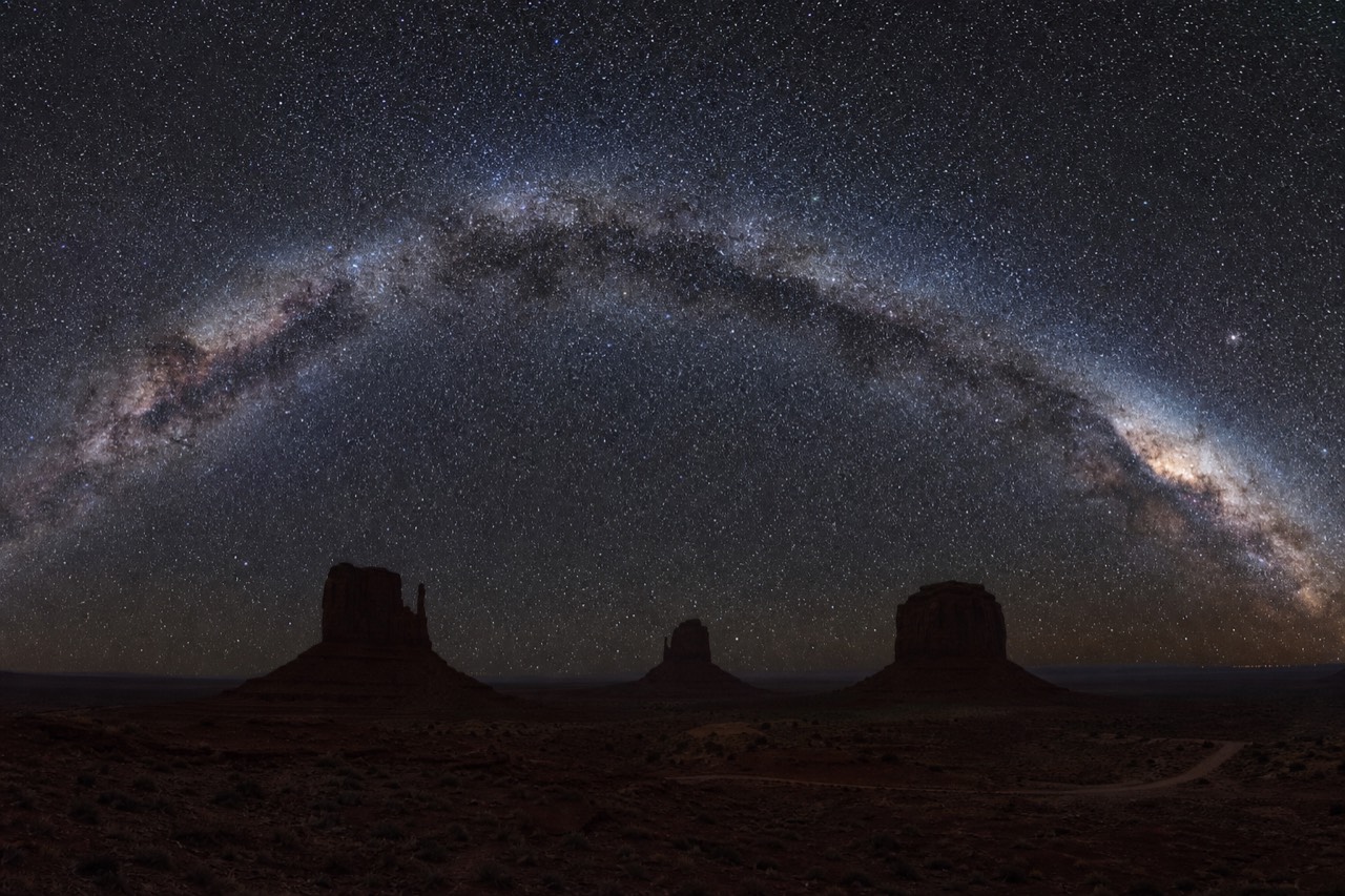 The Milky Way arching over the silhouetted buttes of Monument Valley on a clear night