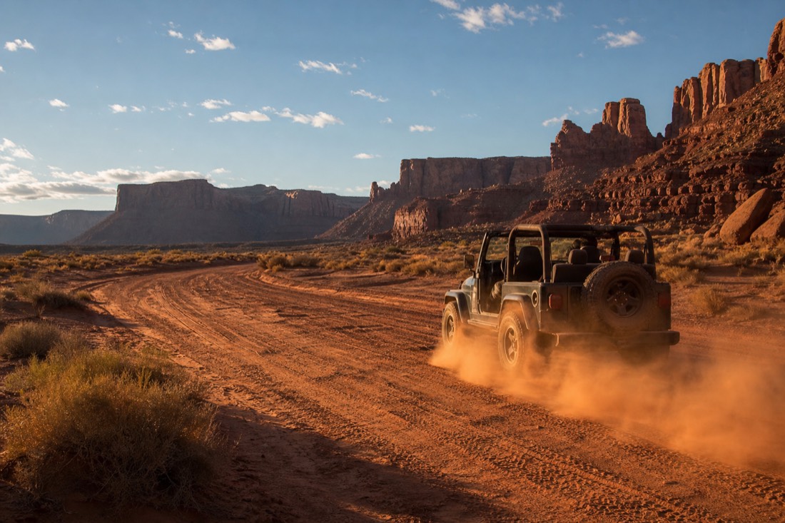 A plume of red dust trailing behind an open jeep on the washboard sand of the Valley Drive under high desert sun