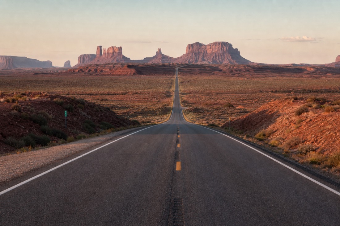 US-163 running dead straight toward the distant buttes at Forrest Gump Point in low sunrise light