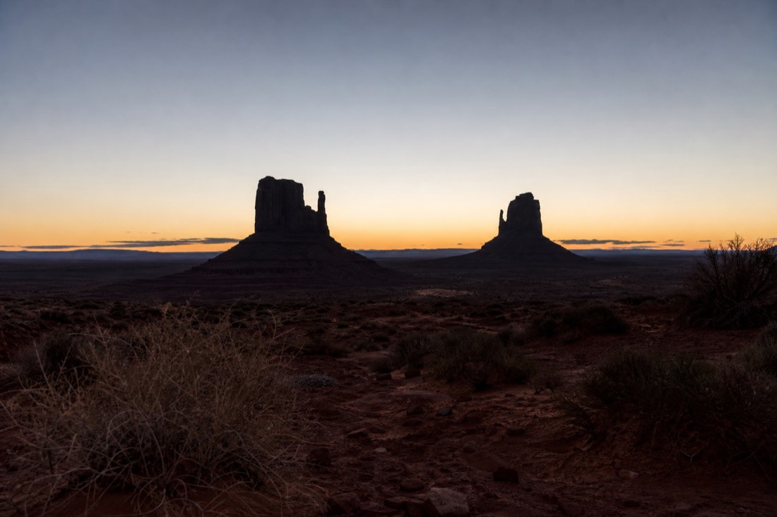The Mitten Buttes as dark silhouettes against a pale pre-dawn sky over Monument Valley