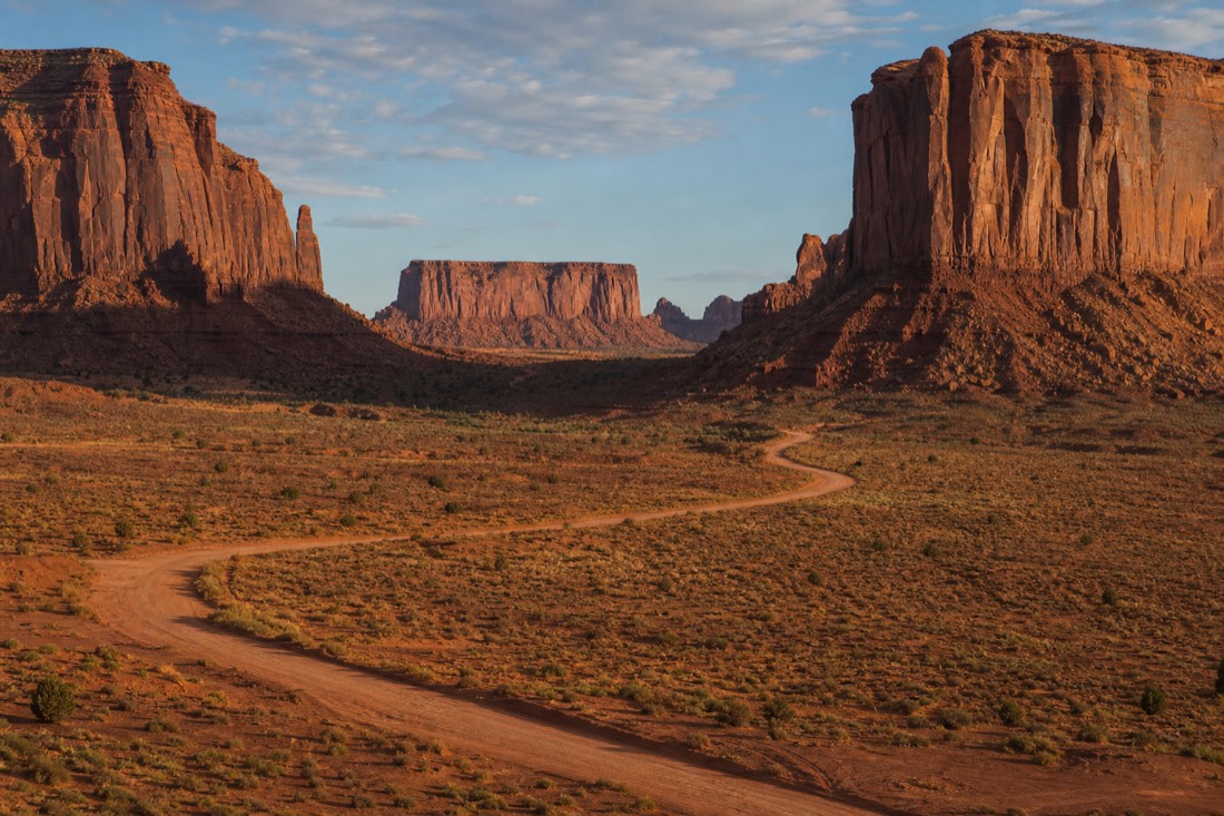 The red dirt Valley Drive loop road curving across the open desert floor between towering sandstone buttes