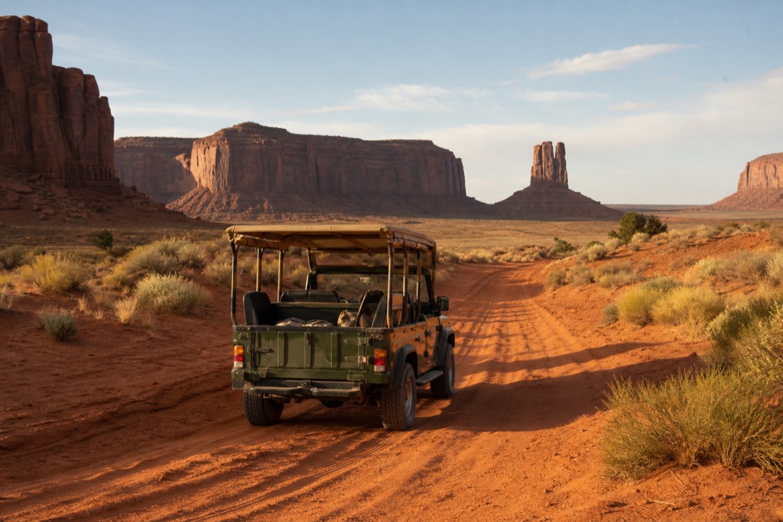 An open-air touring jeep crossing deep red sand on a rough backcountry track deep in Monument Valley