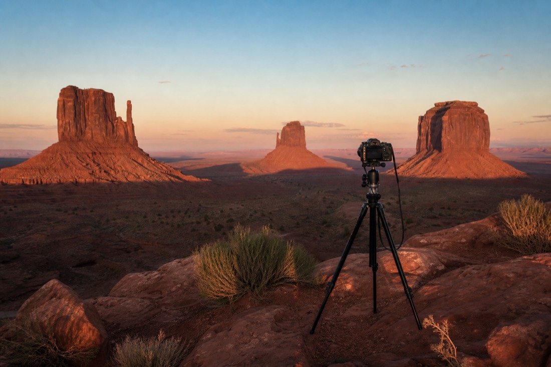 A photographer on a tripod at John Ford Point framing the buttes in golden low-angle autumn light