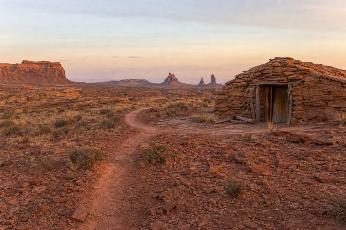 Sandy backcountry track winding past a hogan toward distant buttes in Mystery Valley
