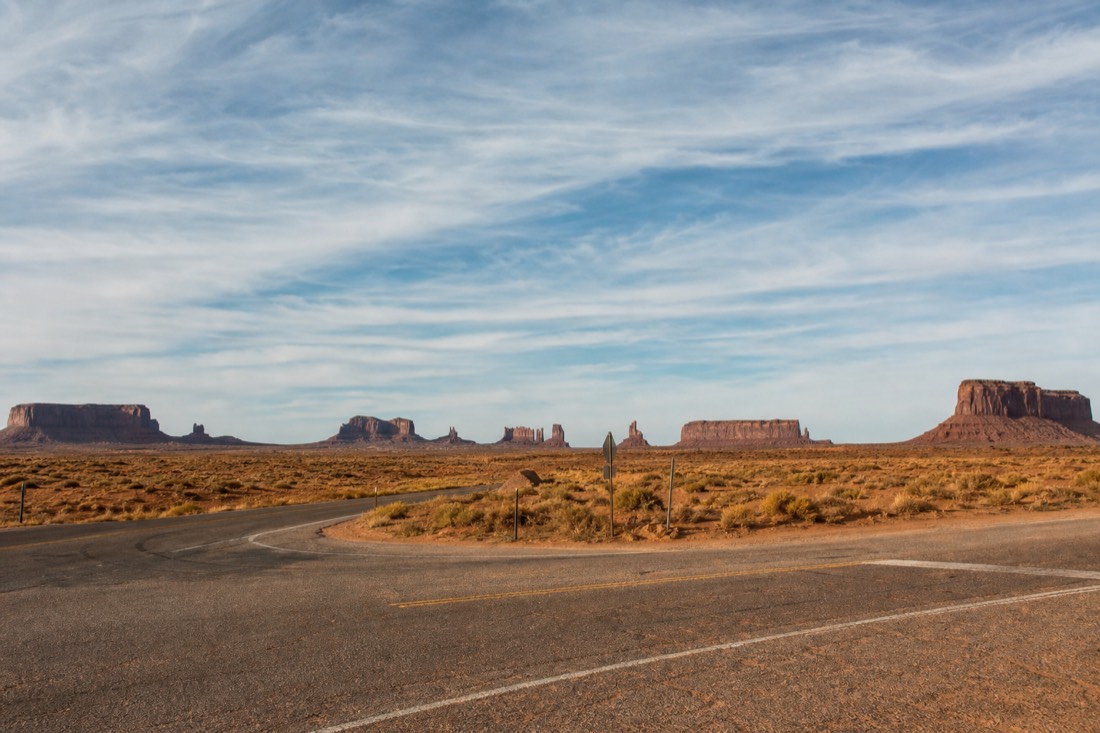 A quiet desert highway junction under a huge sky with Monument Valley's buttes low on the horizon
