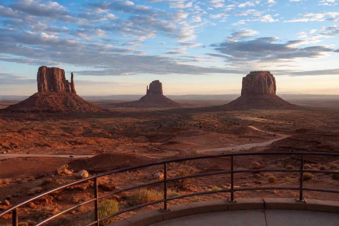 The classic view of the two Mitten buttes and Merrick Butte from the visitor center overlook at warm morning light, empty terrace rail in foreground