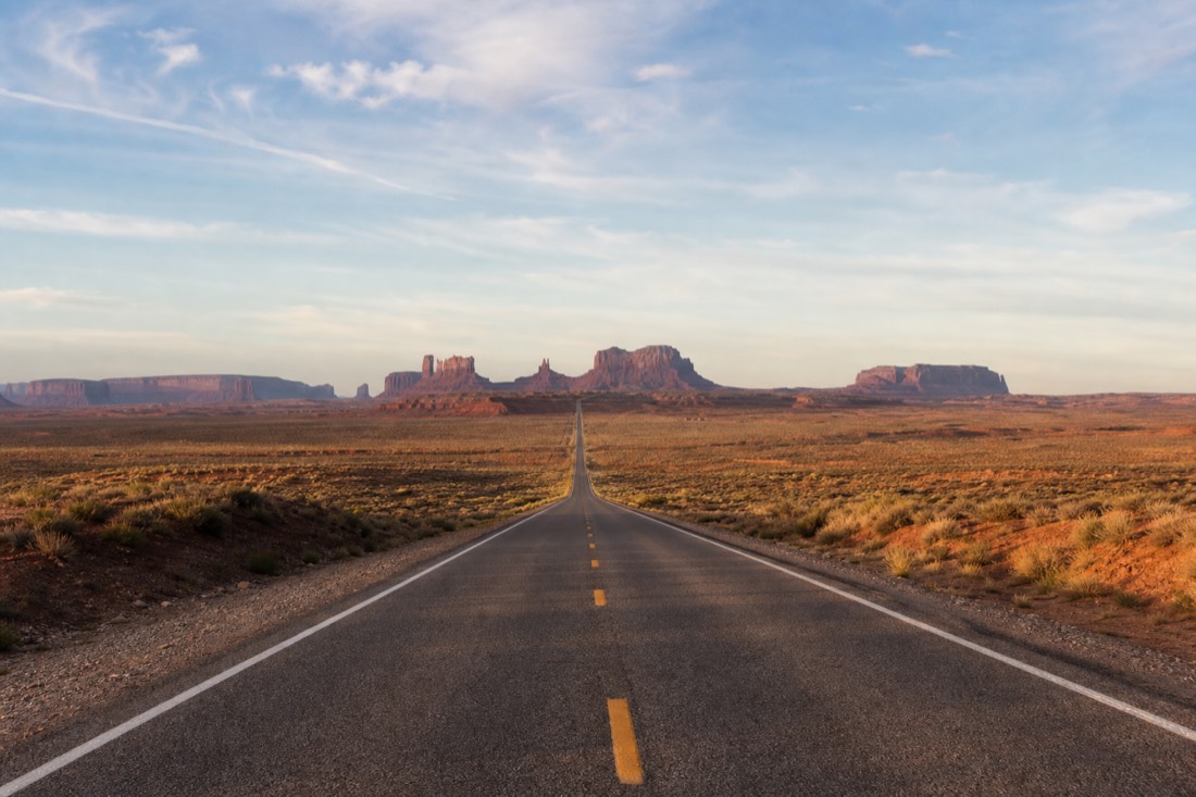 US-163 running dead straight toward Monument Valley's lined-up buttes from the classic northern viewpoint