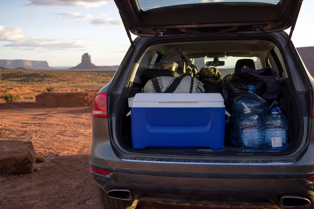 A packed cooler and water jugs loaded in an open car trunk at a high-desert pullout near Monument Valley