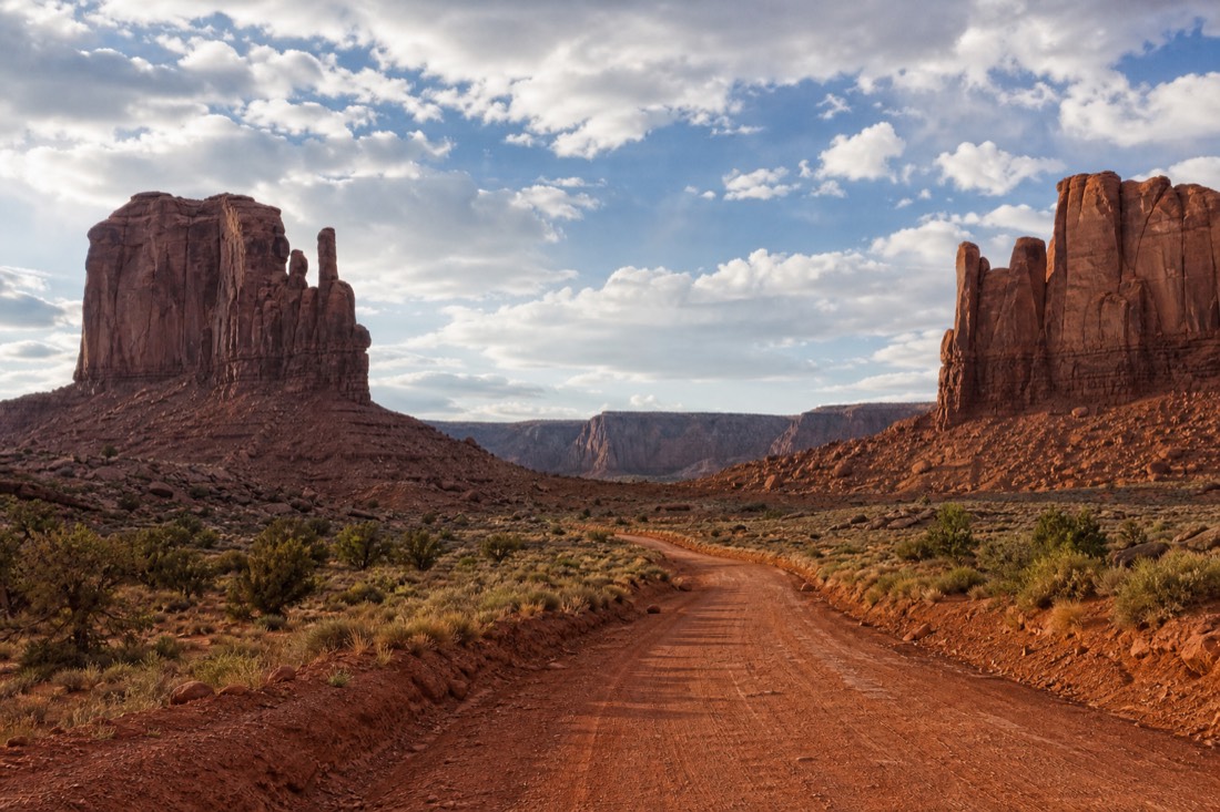 Empty red dirt Valley Drive winding between the mittens under scattered spring clouds