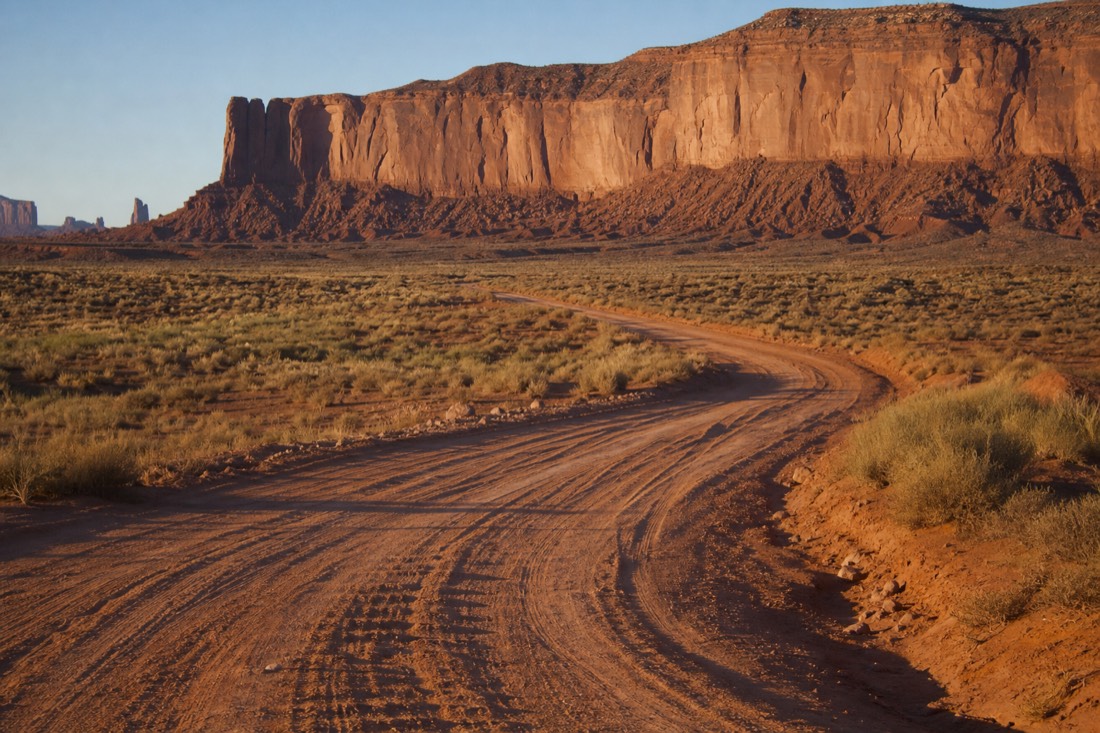 Washboarded red dirt loop road curving through deep sand below towering buttes