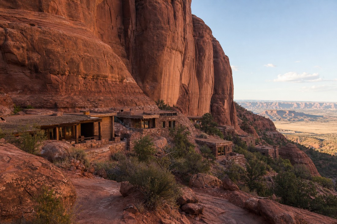 Goulding's-style lodge buildings tucked beneath tall red sandstone cliffs with the distant valley beyond